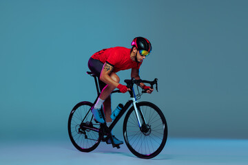 Studio shot of professional cyclist in red sports uniform, goggles and a helmet on a blue background. Concept of active life, rest, travel, energy, sport