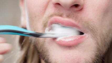 A young guy carefully cleans his teeth with toothpaste and a toothbrush close-up. Boy with young stubble