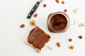 Bread with chocolate paste. A jar of chocolate paste, a knife and various types of nuts. Cashew, almond, walnut, hazelnut, isolated on white background.