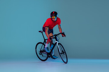 Fototapeta na wymiar Studio shot of professional cyclist in red sports uniform, goggles and a helmet on a blue background. Concept of active life, rest, travel, energy, sport