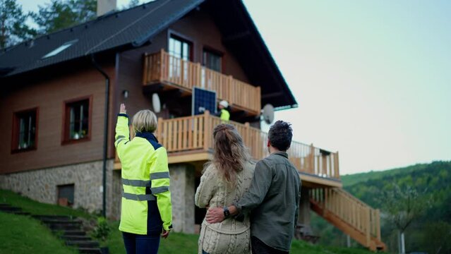Woman engineer talking to couple about solar panel installation in front of their house.