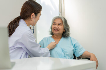 Fototapeta premium Physician examining heart with a stethoscope and talking with a senior woman at a clinic for check yearly checkup, Medicine health care service and medical insurance concept.