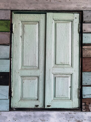 Old grunged wooden window frame painted white vintage with old colourful plywood wall. Antique window frame and old panes. Old closed window and planks of old wooden house. Background of wooden walls