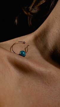 Vertical shot of an earring with a turquoise stone on a tender collarbone of a woman