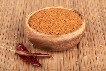 Ground red pepper in a wooden bowl and dry pepper pods on a bamboo mat.