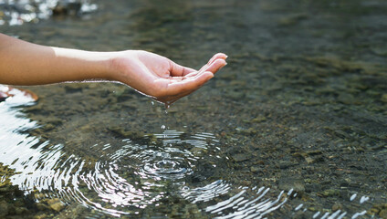 Man's hand touching water in the midst of nature