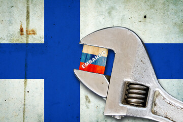 Embargo. Word on a wooden block in the colors of the Russian flag. Clamped wrench. Against the background of the flag of Finland. Business. Politics.