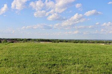 The grass field with the white clouds in the blue sky.