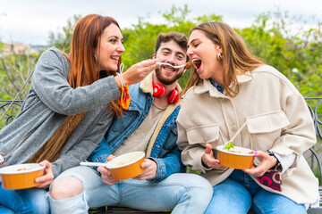 Young people eating take away food at city park - Happy young friends eating takeaway food outdoor...