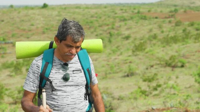 Medium shot of middle aged man with travel backpack climbing mountian with support stick - concept of active lifestyle, exploration and adventures