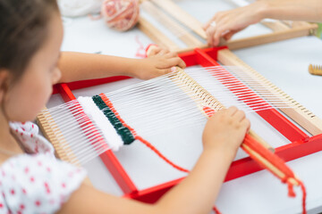 Girl weaving small rug with pattern at masterclass on weaving. Girl is studying how to weave on manual table loom. Process of creation. Handmade concept