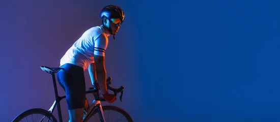 Schilderijen op glas One male cyclist riding bicycle wearing cycling shorts and protective helmet isolated on dark blue background in neon. Concept of sport, speed, energy © master1305