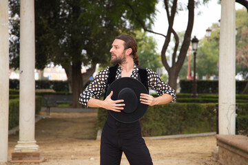 gypsy man dancing flamenco with long hair and beard in a park next to some marble columns. He is...