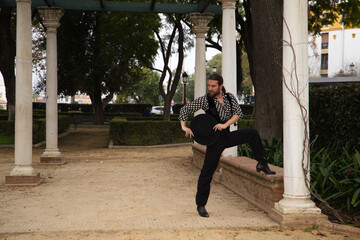 gypsy man dancing flamenco with long hair and beard in a park next to some marble columns. He is...