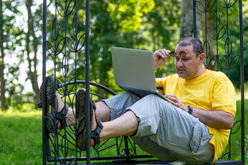 senior man with laptop working outside in garden, green home office concept.