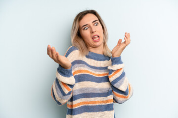 young adult pretty woman shrugging with a dumb, crazy, confused, puzzled expression, feeling...