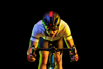 Portrait of professional male cyclist in sports uniform, goggles and helmet on dark background in...