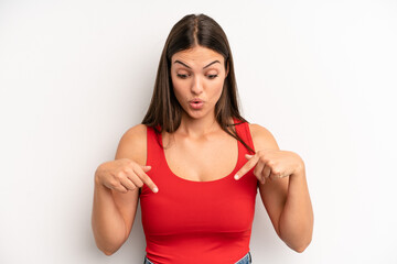 young adult pretty woman feeling shocked, open-mouthed and amazed, looking and pointing downwards...