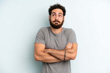 young adult bearded man shrugging, feeling confused and uncertain, doubting with arms crossed and puzzled look