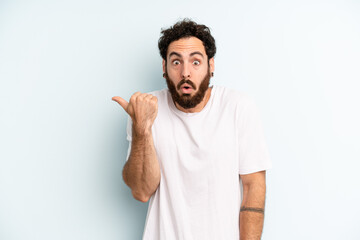 young adult bearded man looking astonished in disbelief, pointing at object on the side and saying...