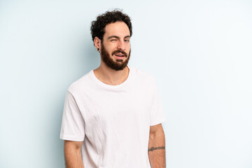 young adult bearded man looking happy and friendly, smiling and winking an eye at you with a...