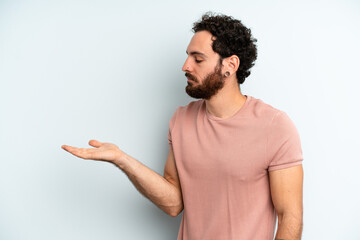 young adult bearded man feeling happy and smiling casually, looking to an object or concept held on...