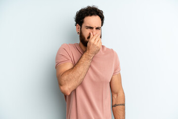 young adult bearded man feeling disgusted, holding nose to avoid smelling a foul and unpleasant...