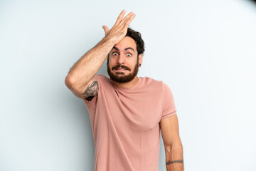 young adult bearded man raising palm to forehead thinking oops, after making a stupid mistake or...