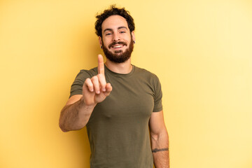 young adult bearded man smiling and looking friendly, showing number one or first with hand forward, counting down © kues1