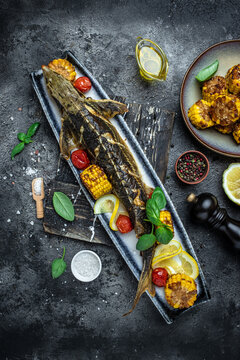 Grilled Sturgeon fish with vegetables, lemon, herbs and spices on a dark background, vertical image. top view. place for text