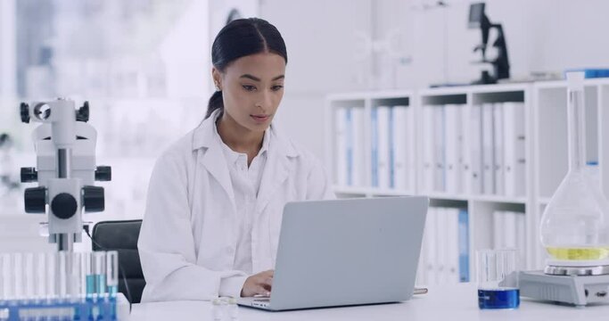 Young researcher or biologist thinking of new innovative studies to develop medical research. Biotechnology chemist looking at statistics results. Female scientist working on a laptop in a modern lab