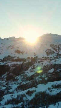 Vertical drone footage of the snow-covered mountains with the sunrays coming from behind