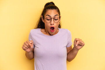hispanic pretty woman feeling shocked, open-mouthed and amazed, looking and pointing downwards in...