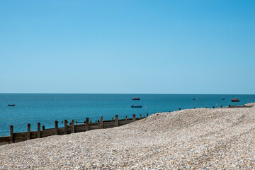 deserted beach with bank of pebbles and sea and sky in the background with fishing boats