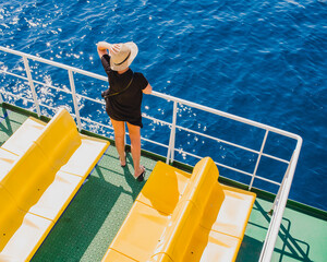 Beautiful sea voyage in the rays of the sun. A young woman in a straw hat stands on the deck of a ship and looks at the sea.