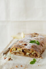 Freshly baked homemade apple pie with powdered sugar and mint leaves, composition on a white background, traditional puff pastry strudel with apple. 