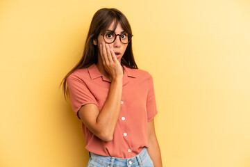 hispanic pretty woman feeling shocked and astonished holding face to hand in disbelief with mouth...