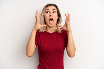 young adult blonde woman screaming with hands up in the air, feeling furious, frustrated, stressed and upset