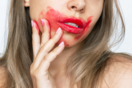 Cropped shot of a young caucasian blonde woman with perfect lips smearing glossy red color lipstick on the face with her hand isolated on a white background. Beauty and fashion concept
