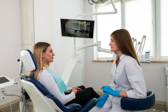 She is sitting in the dentist's chair. The dentist explains and advises the patient.
