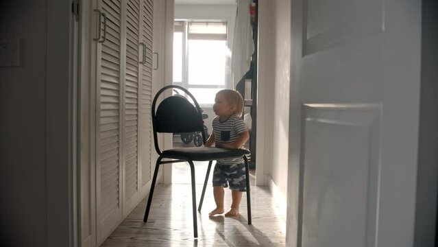 A little baby boy drags a chair among the corridor and crawls on it