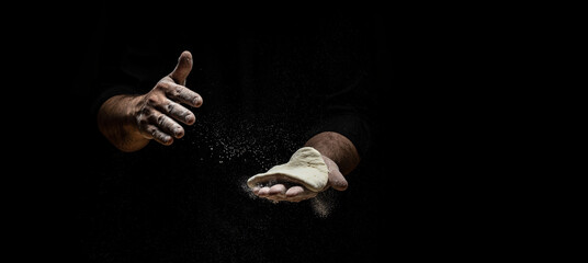 Beautiful and strong men's hands knead the dough from which they will then make bread, pasta or pizza. A cloud of flour flies around like dust. Food concept