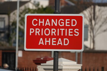 A red sign stating Changed Priorities Ahead. 