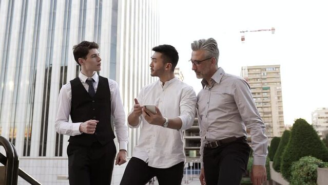 Diverse male business people walking holding folder with documents communicate before meeting, discuss