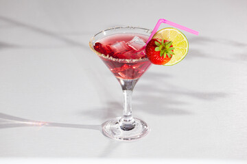 Red sweet cold party drink in elegant shot glass with ice cubes, strawberry and lime