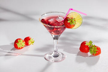Red sweet cold party drink in elegant shot glass with ice cubes, strawberry and lime