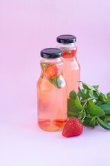 Homemade strawberry mint lemonade in two glass bottles to go. Eco packaging, reusable dishes zero waste concept. Natural healthy alcohol free drink recipe for hot summer on pink background