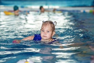 Fototapeta na wymiar Small toddler kid learns to swim with board in pool. Swimming lesson. Active kid plays in water
