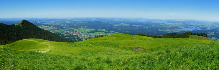 weites Panorama vom Hörnle bei Bad Kohlgrub bis zum Staffelsee über Wiesen, Berge und Wald bei blauem Himmel