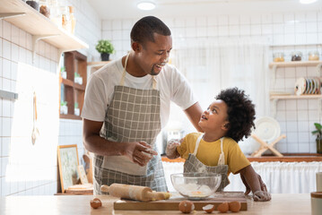Happy smiling Black African American Father and son playing while doing bakery in kitchen at home.
